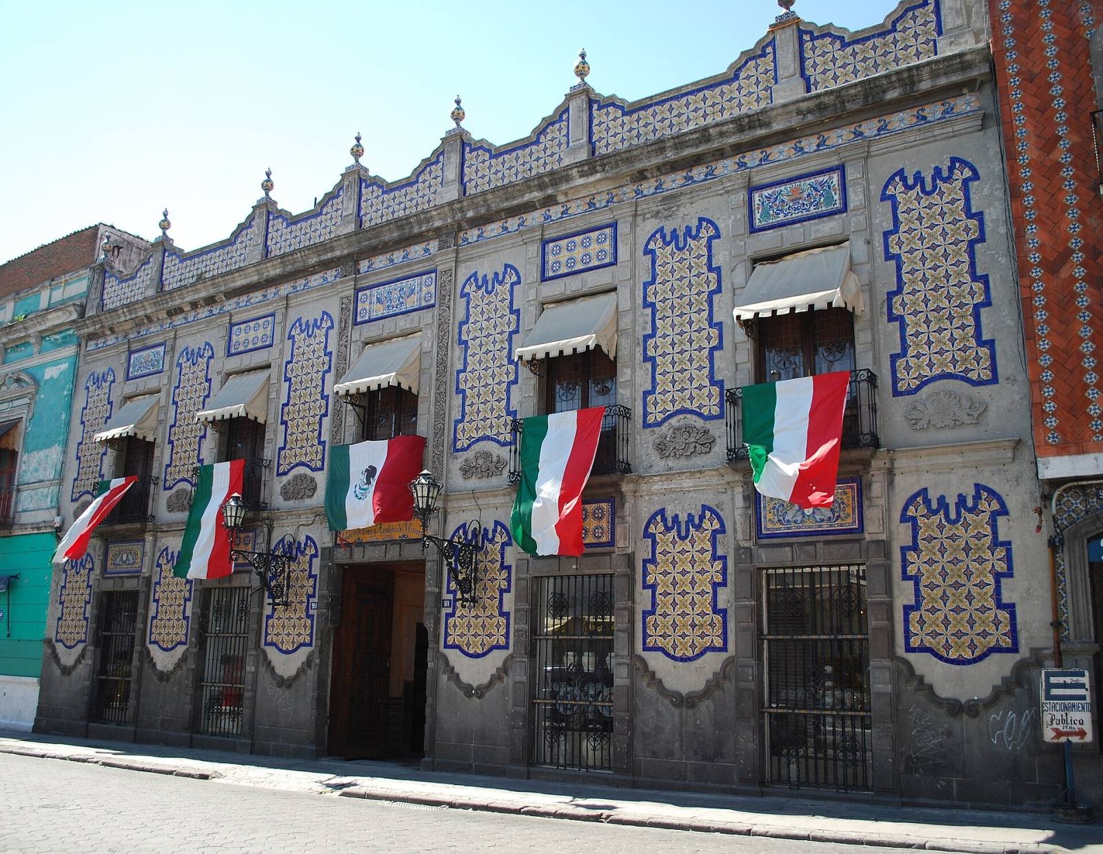 A street front covered in blue and white Talavera tiles, hung with Mexican flags