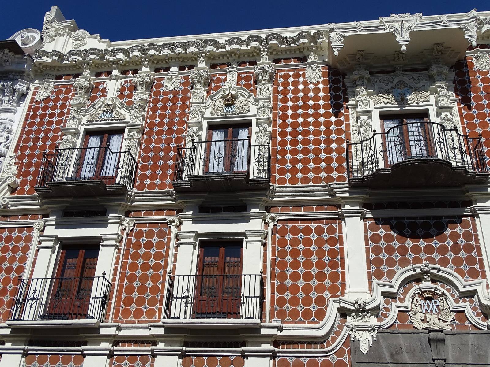 A colonial house front covered in red and white Talavera tiles, with white plaster decoration and iron balconies