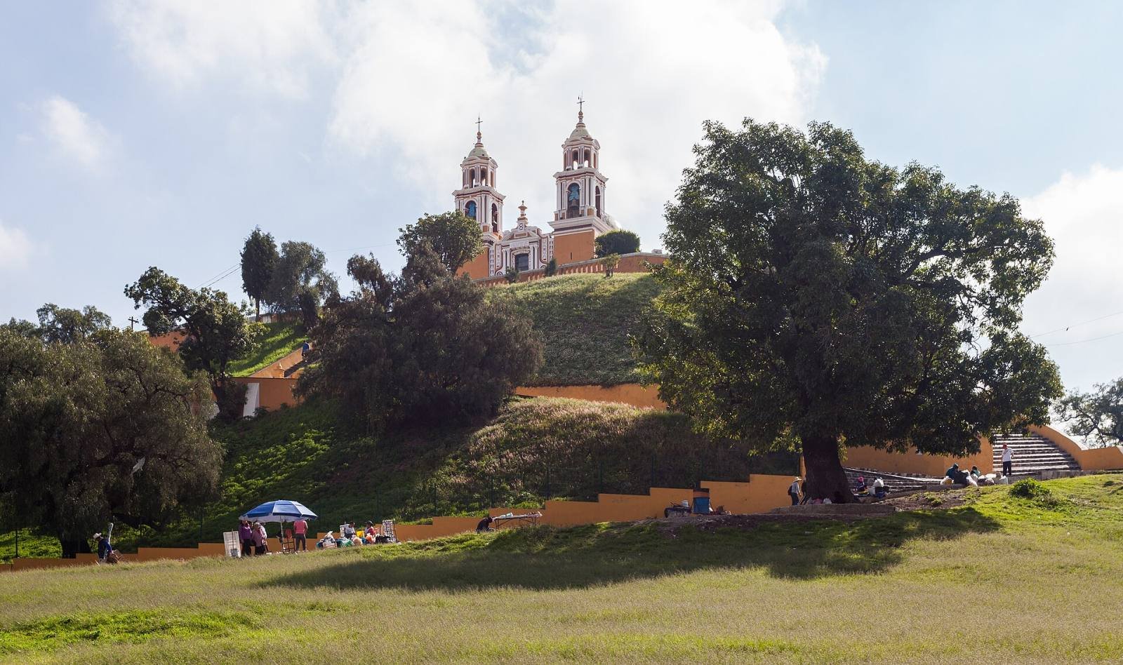 The yellow church of Our Lady of Remedies on top of the Great Pyramid of Cholula, with trees on the slopes