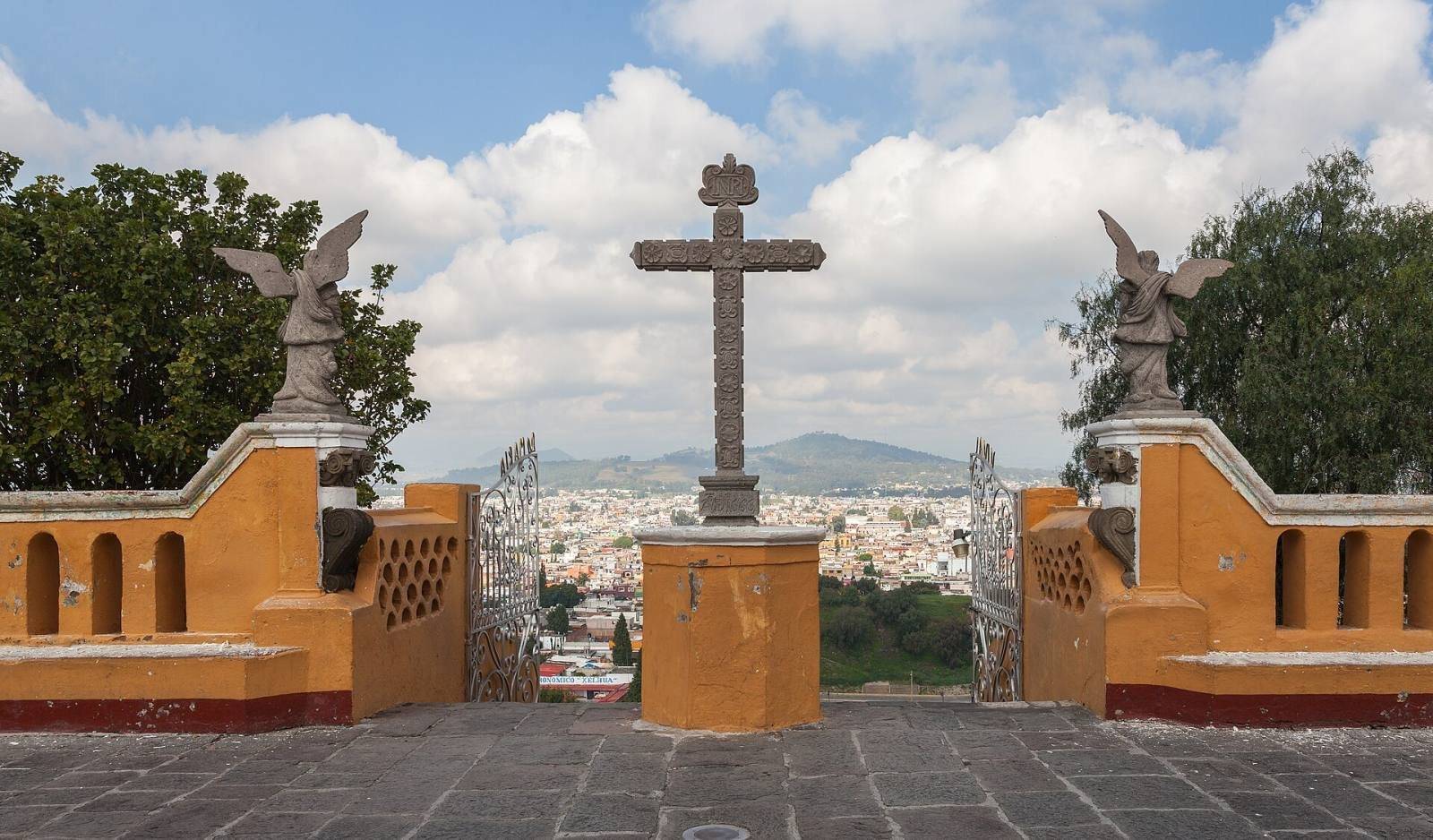 A stone cross in the atrium of the church on top of the Cholula pyramid, with the town spread out below
