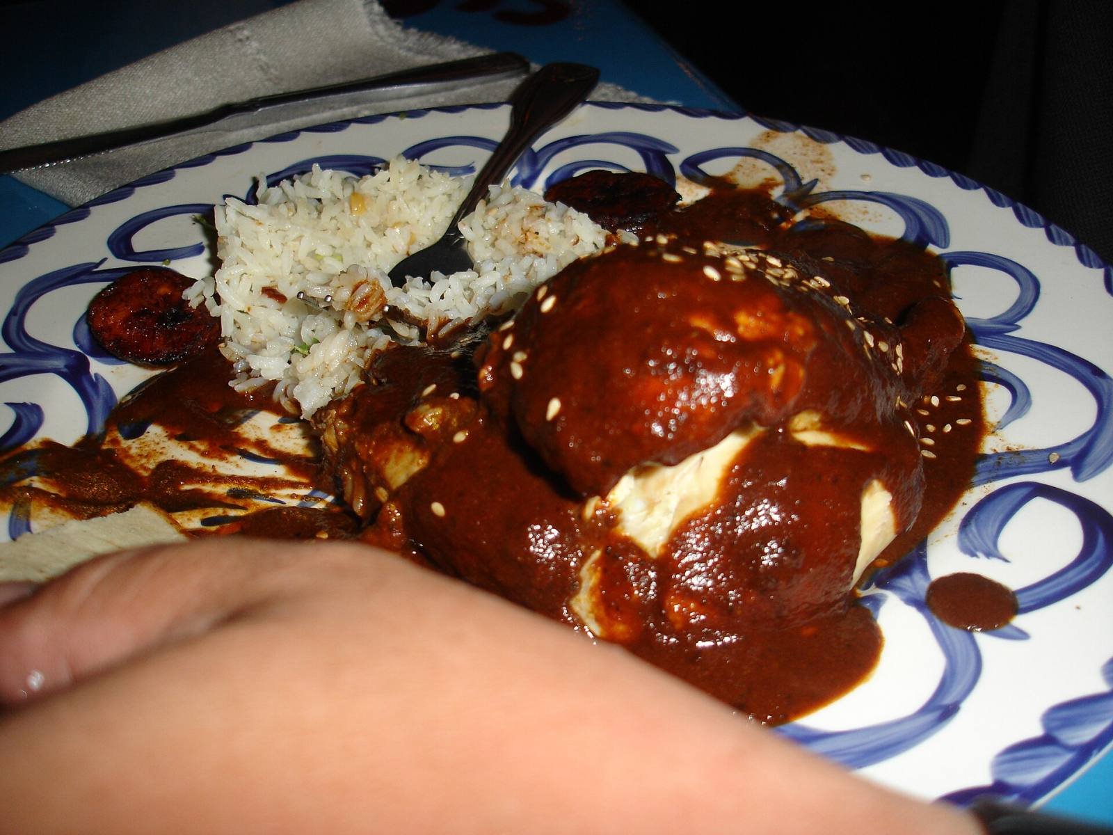 Chicken covered in dark mole poblano with rice on a blue and white plate