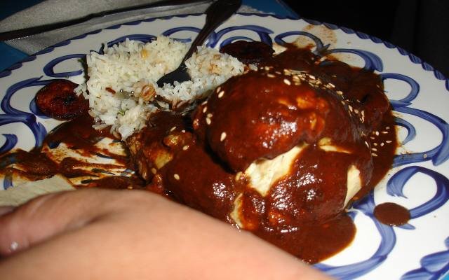 Chicken covered in dark mole poblano with rice on a blue and white plate