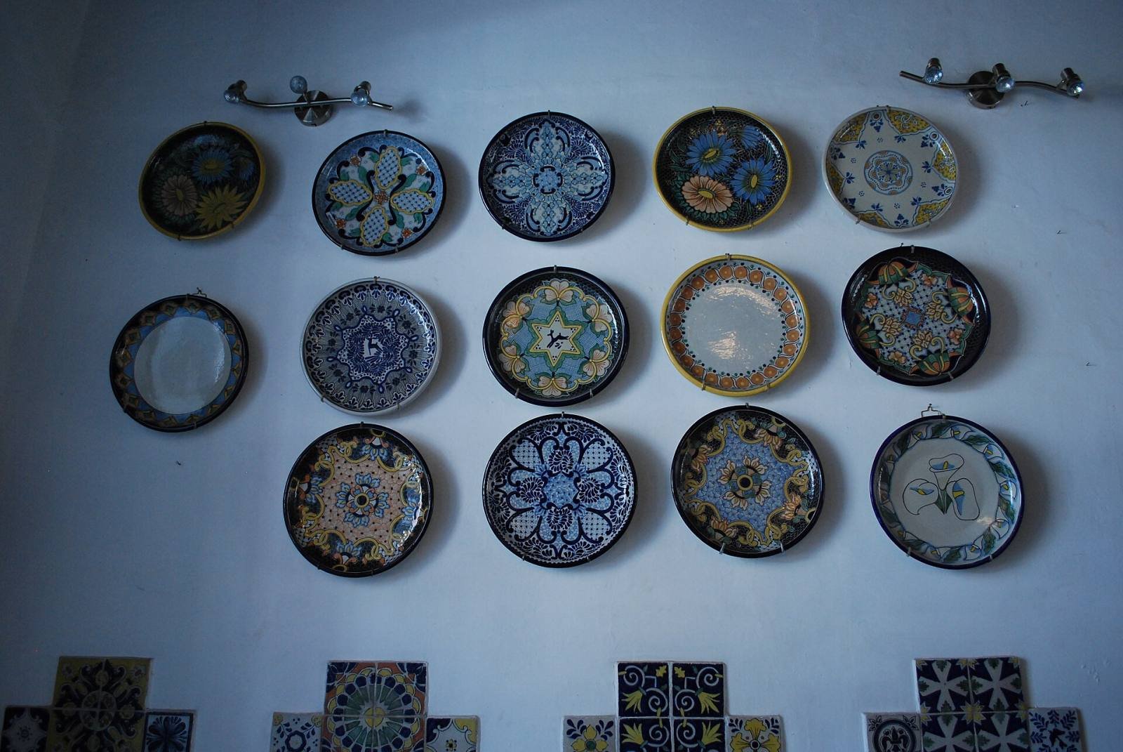 Hand-painted Talavera plates in blue, yellow and green hanging on a white wall