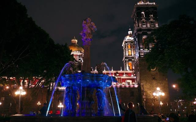 The fountain of the zócalo and the cathedral tower lit up at night